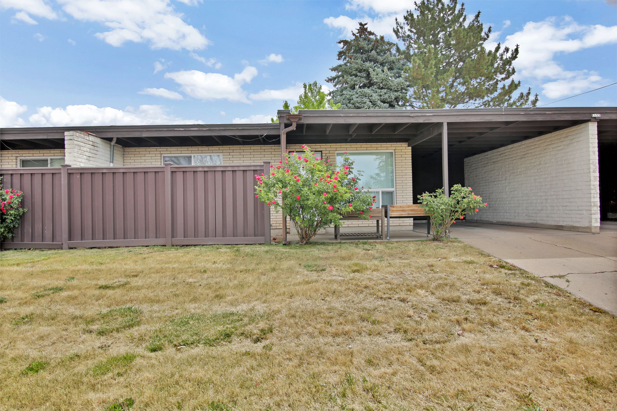 Brick facade residence featuring a covered carport, a private fenced area, and established plantings