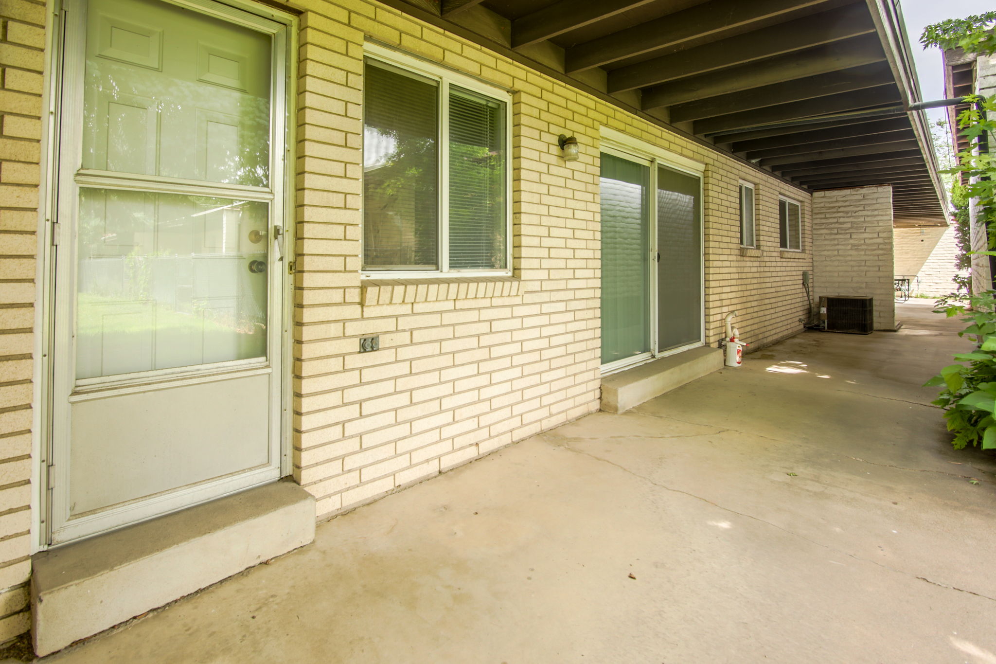 Exterior featuring cream brick facade, a concrete patio, a full-lite storm door, and sliding glass door access