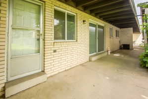 Exterior featuring cream brick facade, a concrete patio, a full-lite storm door, and sliding glass door access
