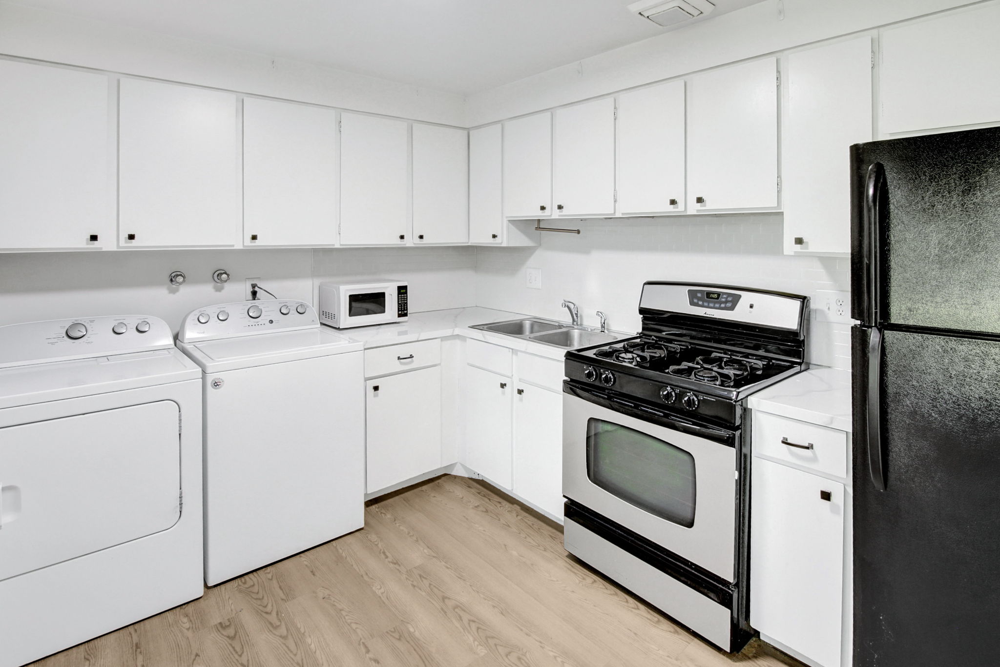 Utility area featuring white cabinetry with black hardware, wood-finish flooring, and a stainless steel gas range