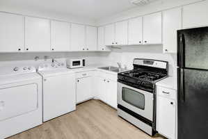 Utility area featuring white cabinetry with black hardware, wood-finish flooring, and a stainless steel gas range