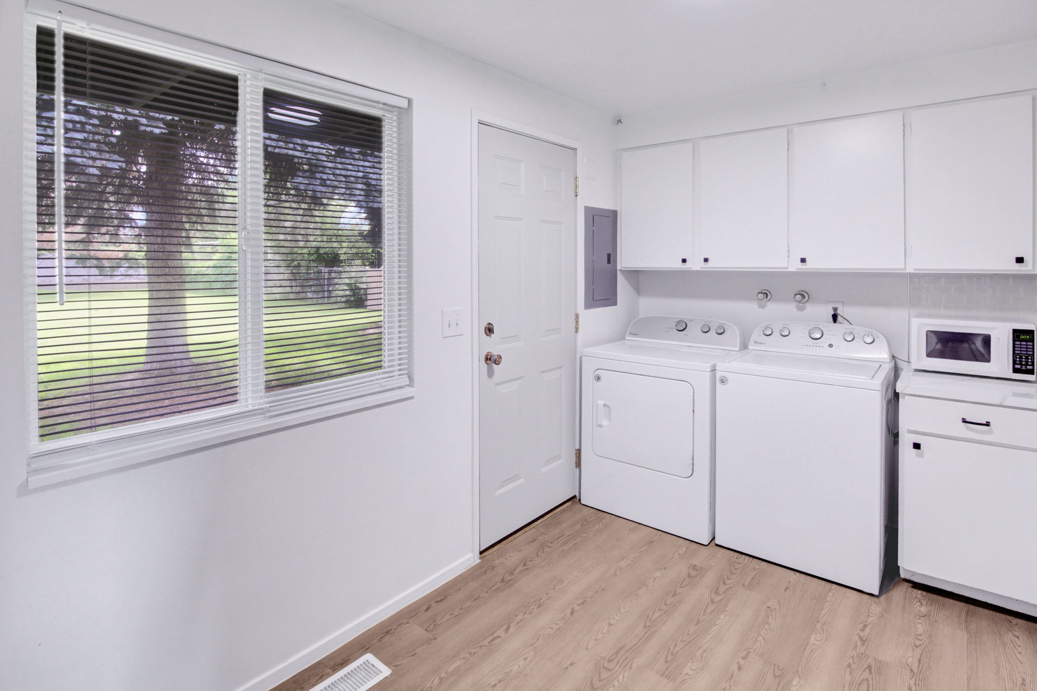 Utility area featuring wood-finish flooring, white cabinetry, and a double window with horizontal blinds
