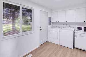 Utility area featuring wood-finish flooring, white cabinetry, and a double window with horizontal blinds