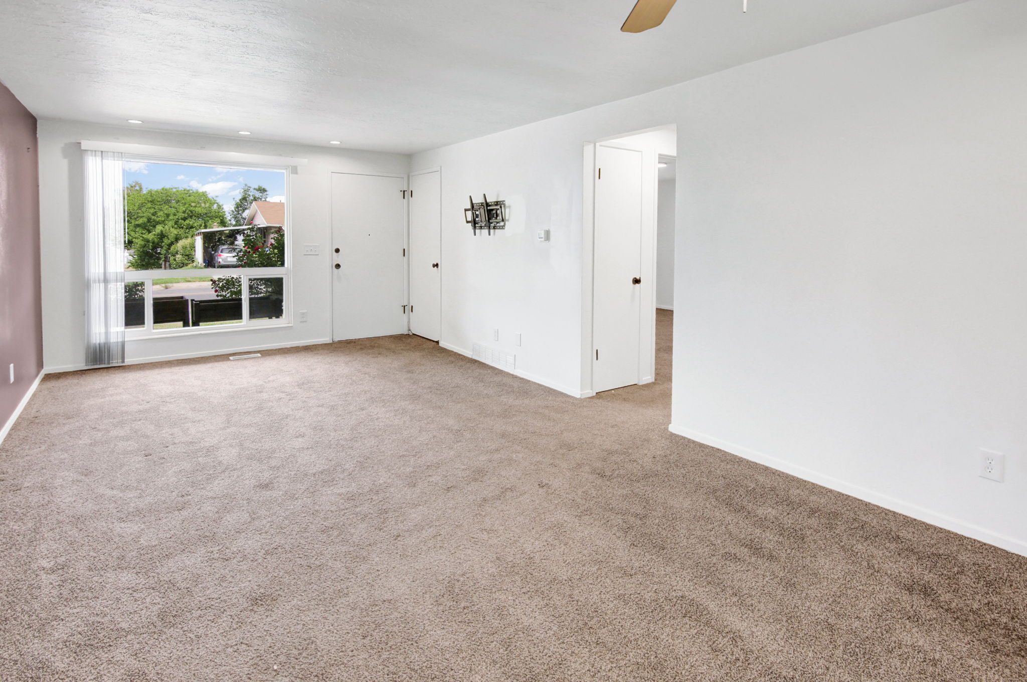Spacious carpeted room featuring a large picture window, recessed lighting, and a neutral color palette