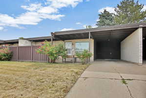 Single-story residence featuring light brick exterior, a carport, concrete driveway, and a fenced yard
