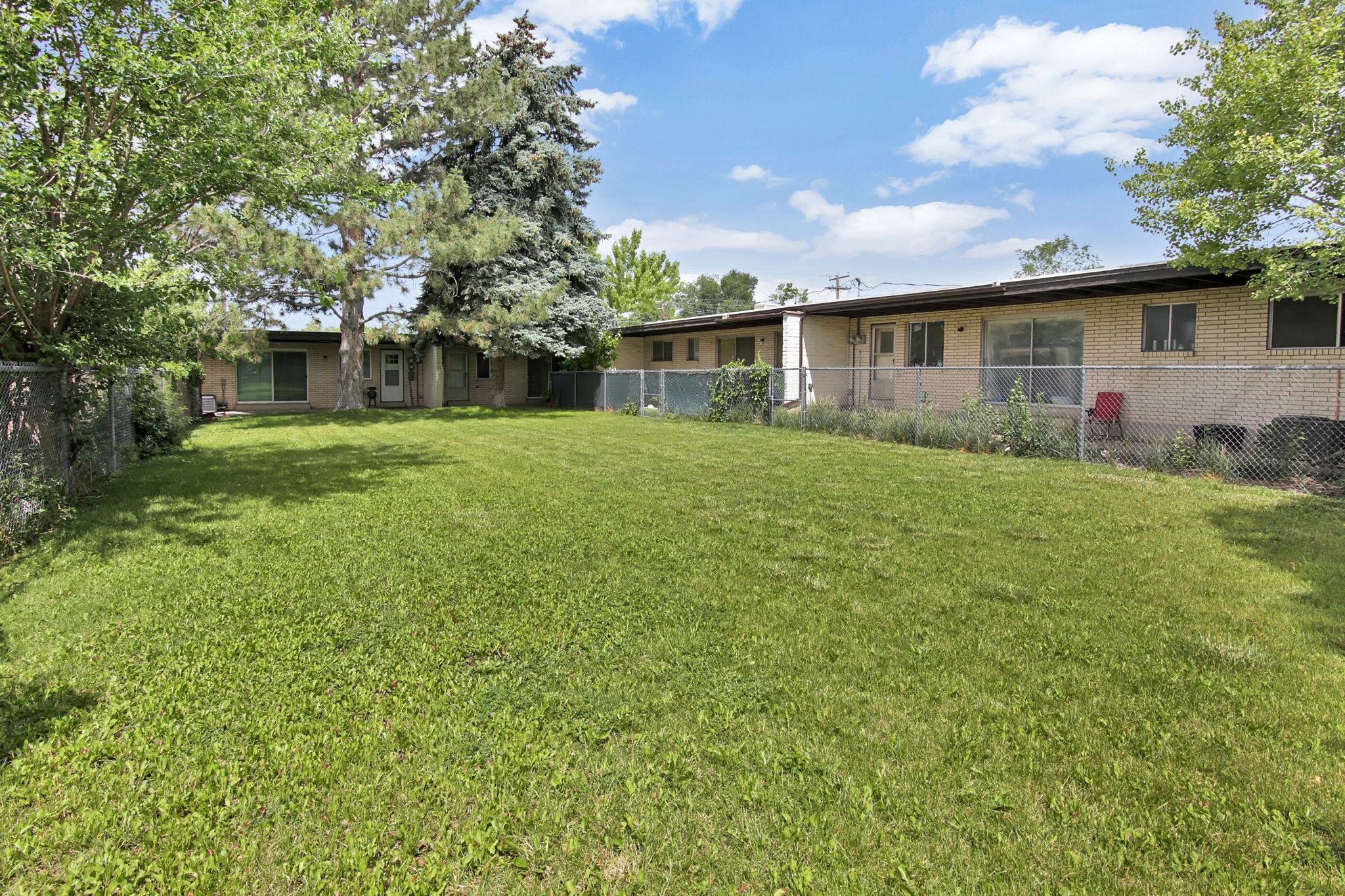 Expansive green lawn with mature trees and a chain-link fence