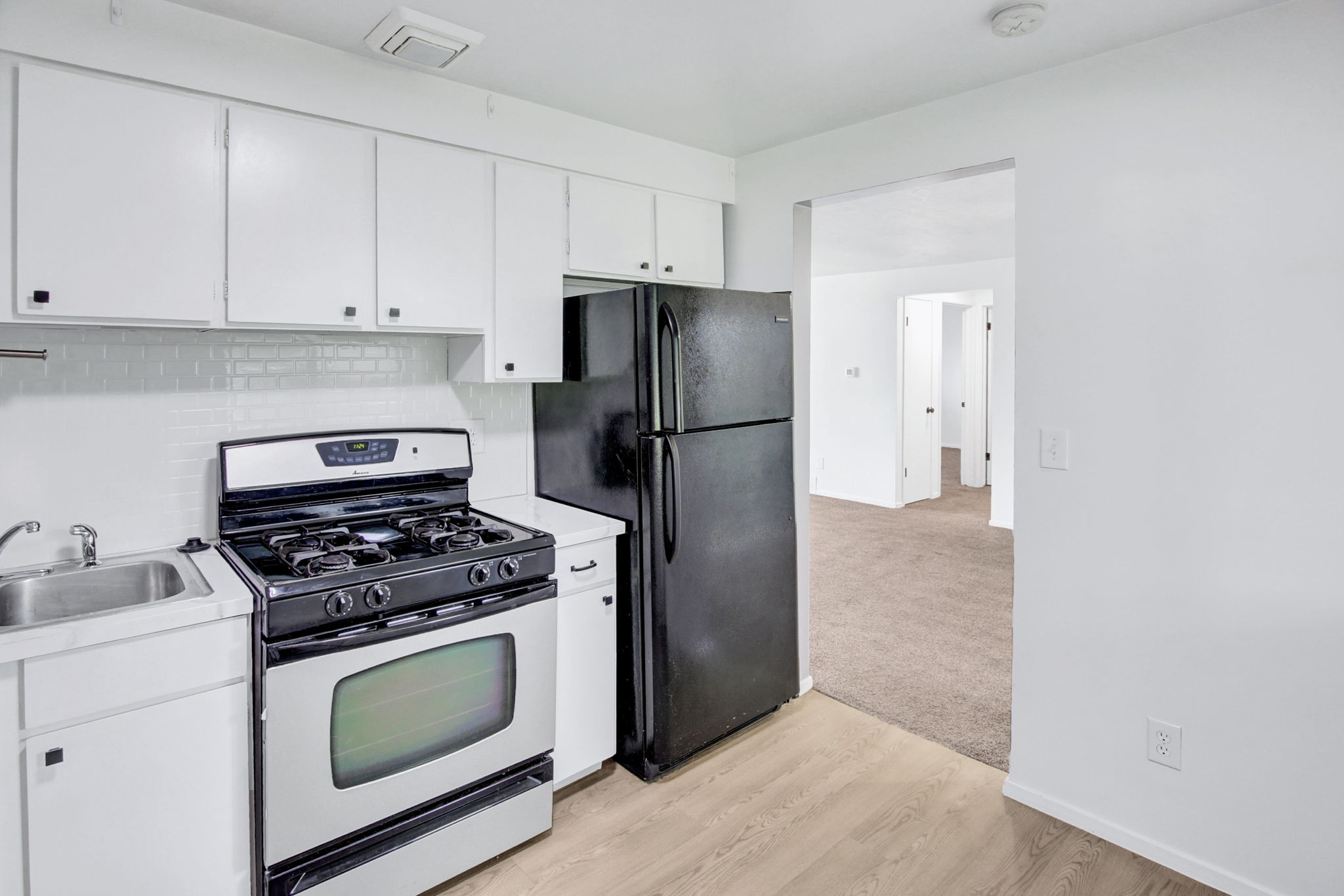 Compact kitchen featuring white cabinetry, a stainless steel gas range, a black refrigerator, and a stainless steel sink