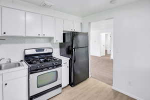 Compact kitchen featuring white cabinetry, a stainless steel gas range, a black refrigerator, and a stainless steel sink