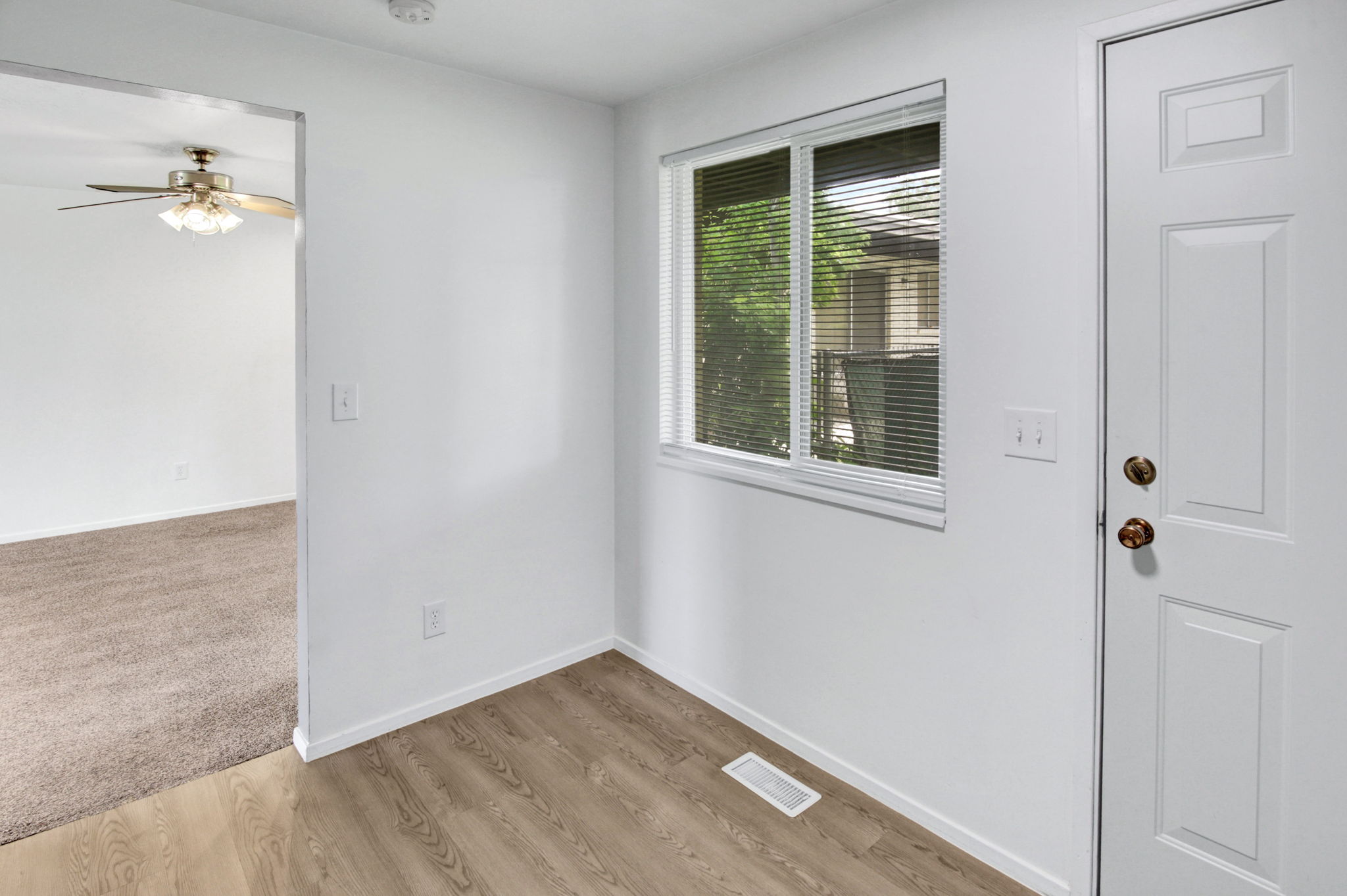 Entryway featuring wood-finish flooring, a white paneled door with brass hardware, and a window with blinds