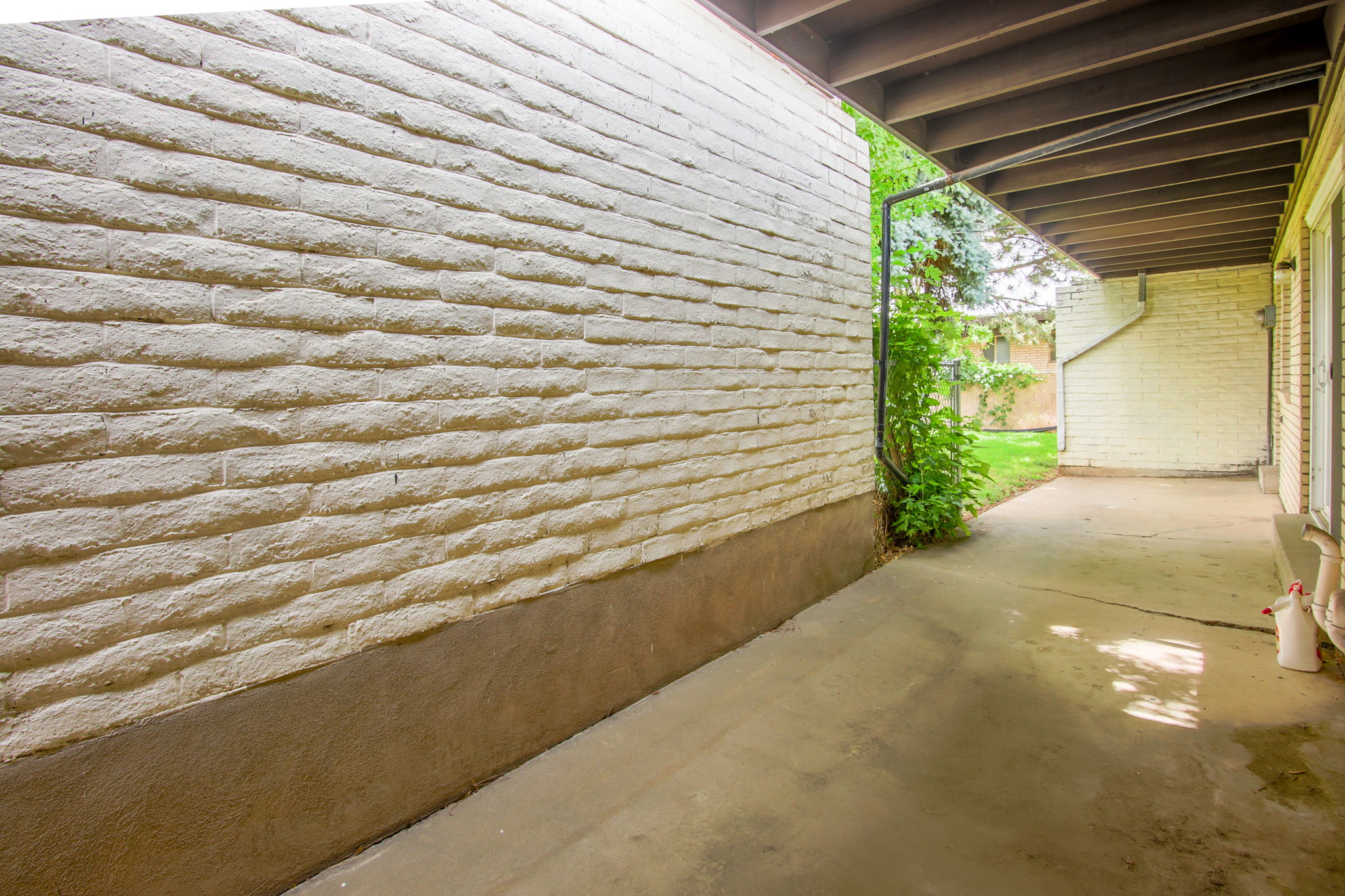 Covered concrete patio with a painted brick wall and exposed wood-beam ceiling