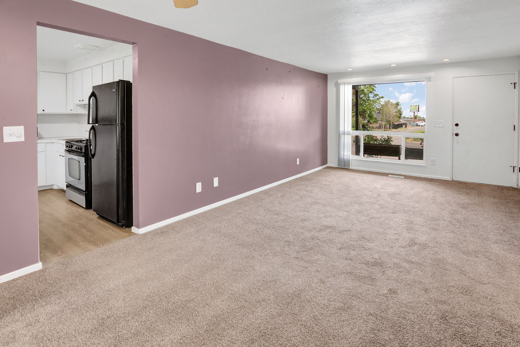 Open living area featuring neutral carpeting, a large picture window, and a white entry door
