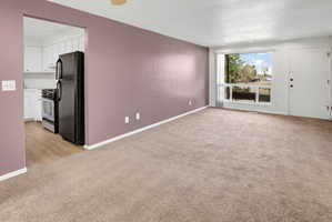 Open living area featuring neutral carpeting, a large picture window, and a white entry door