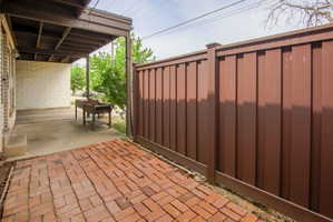 Covered patio area featuring a brick paver section and a solid privacy fence