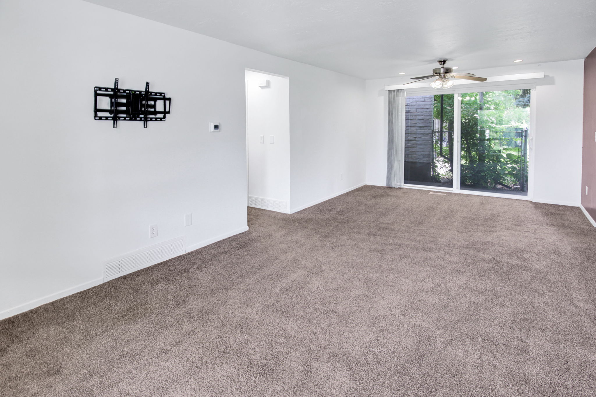 Spacious room featuring neutral carpeting, a glass sliding door, and a ceiling fan with integrated lighting