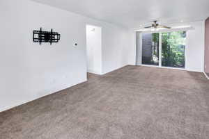 Spacious room featuring neutral carpeting, a glass sliding door, and a ceiling fan with integrated lighting