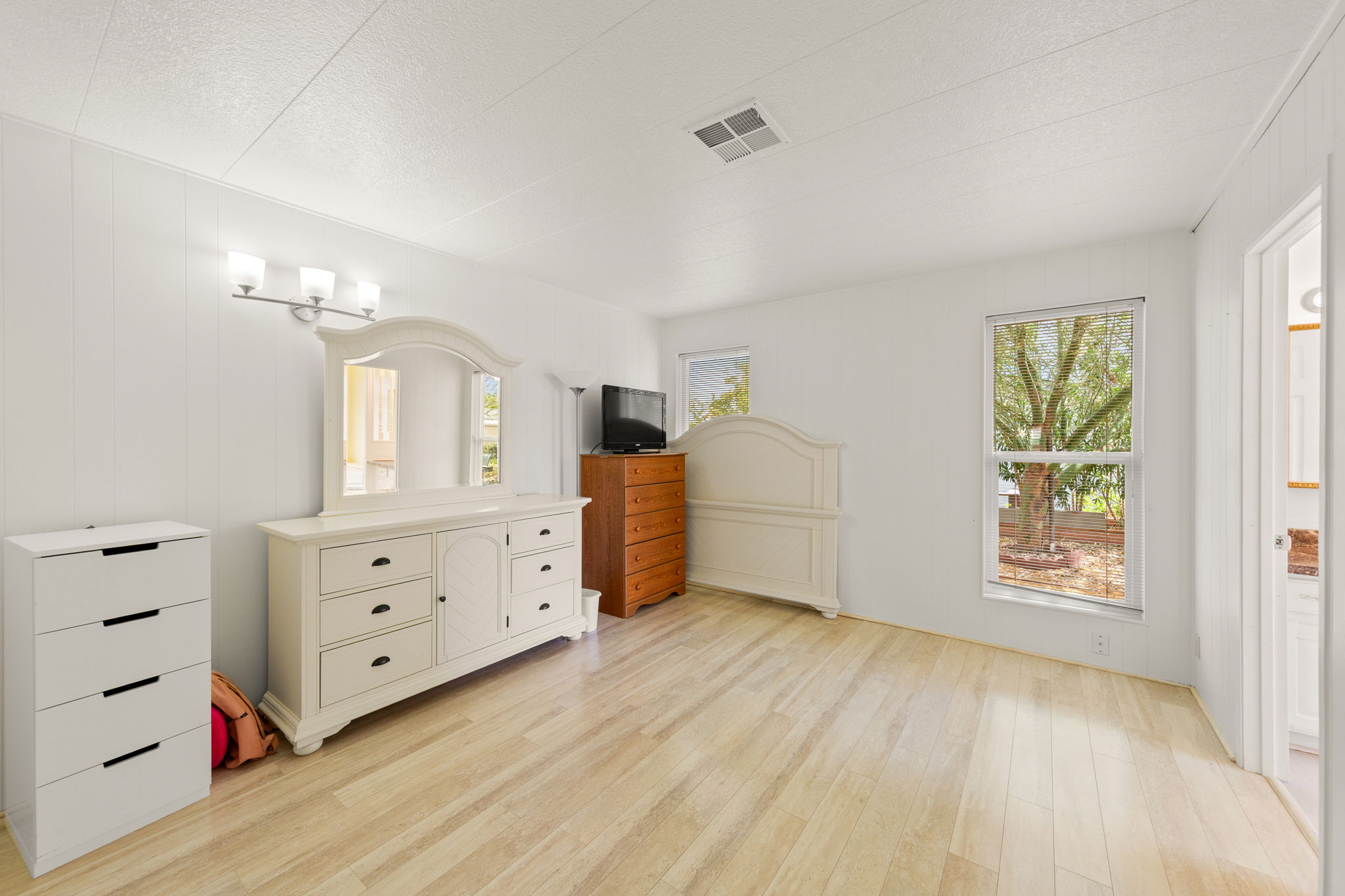 Wood-finish flooring throughout, two windows offering natural light, white paneled walls, and a recessed ceiling vent