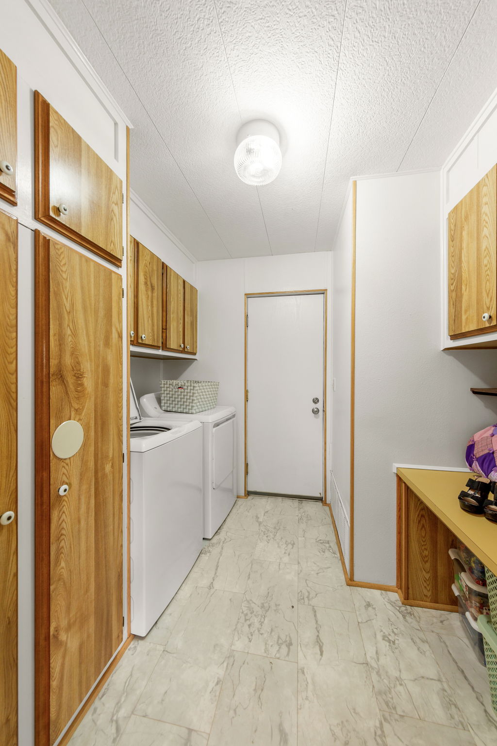 Utility room featuring wood-finish cabinetry, a white door, and light-toned flooring