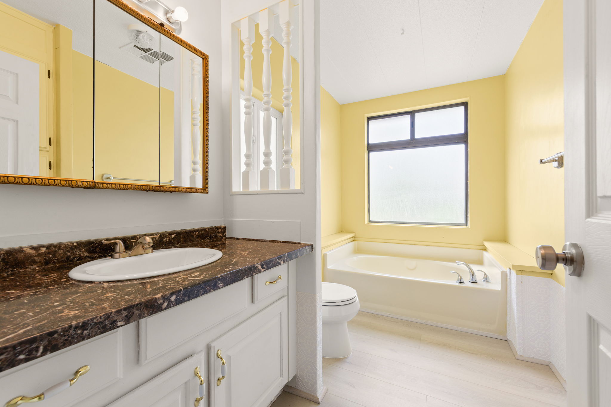Bathroom featuring a vanity with a dark countertop, an oval undermount sink, and white cabinetry with brass-tone hardware