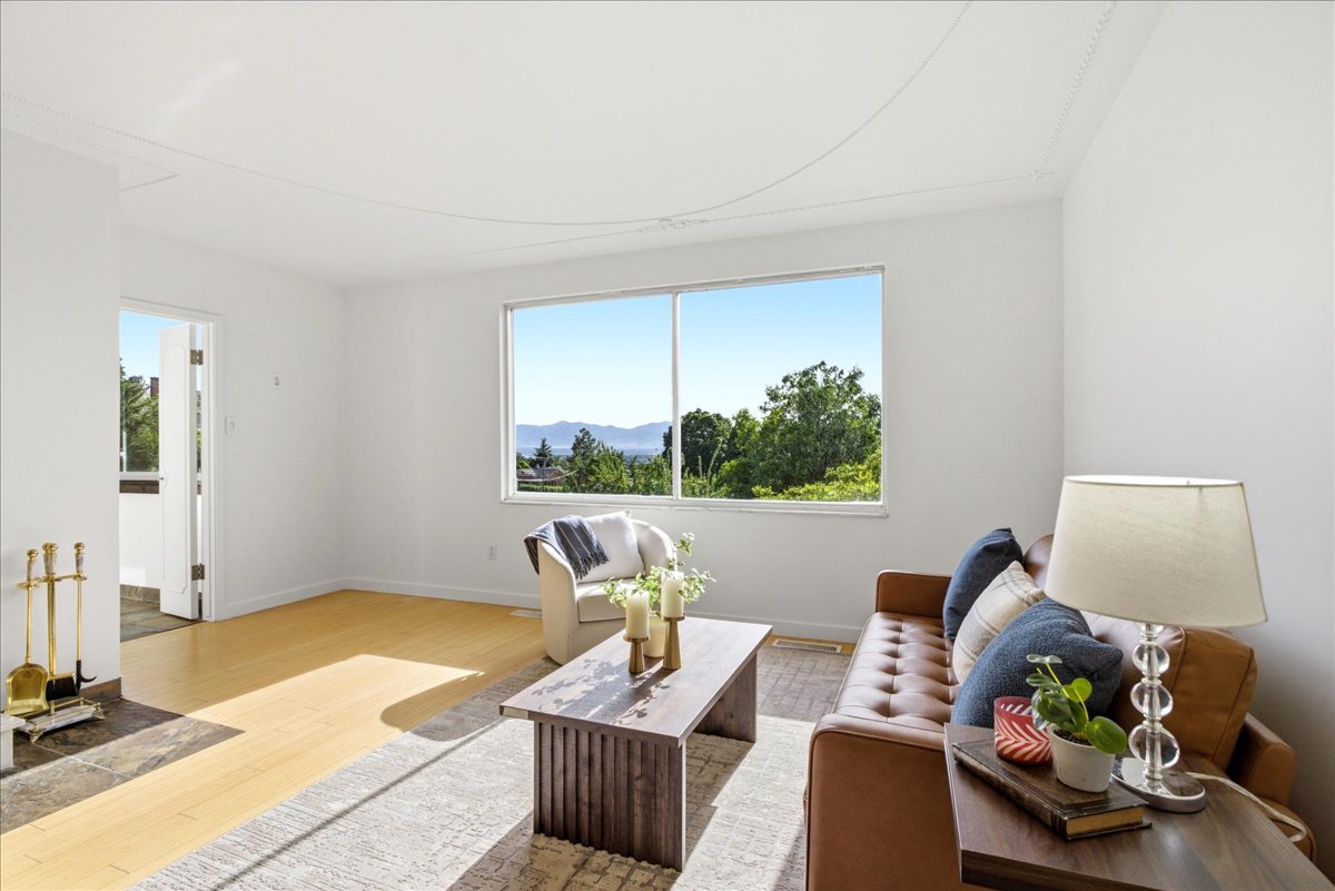 Bright living space featuring a large picture window, light wood-finish flooring, a fireplace with a stone hearth, and white painted walls
