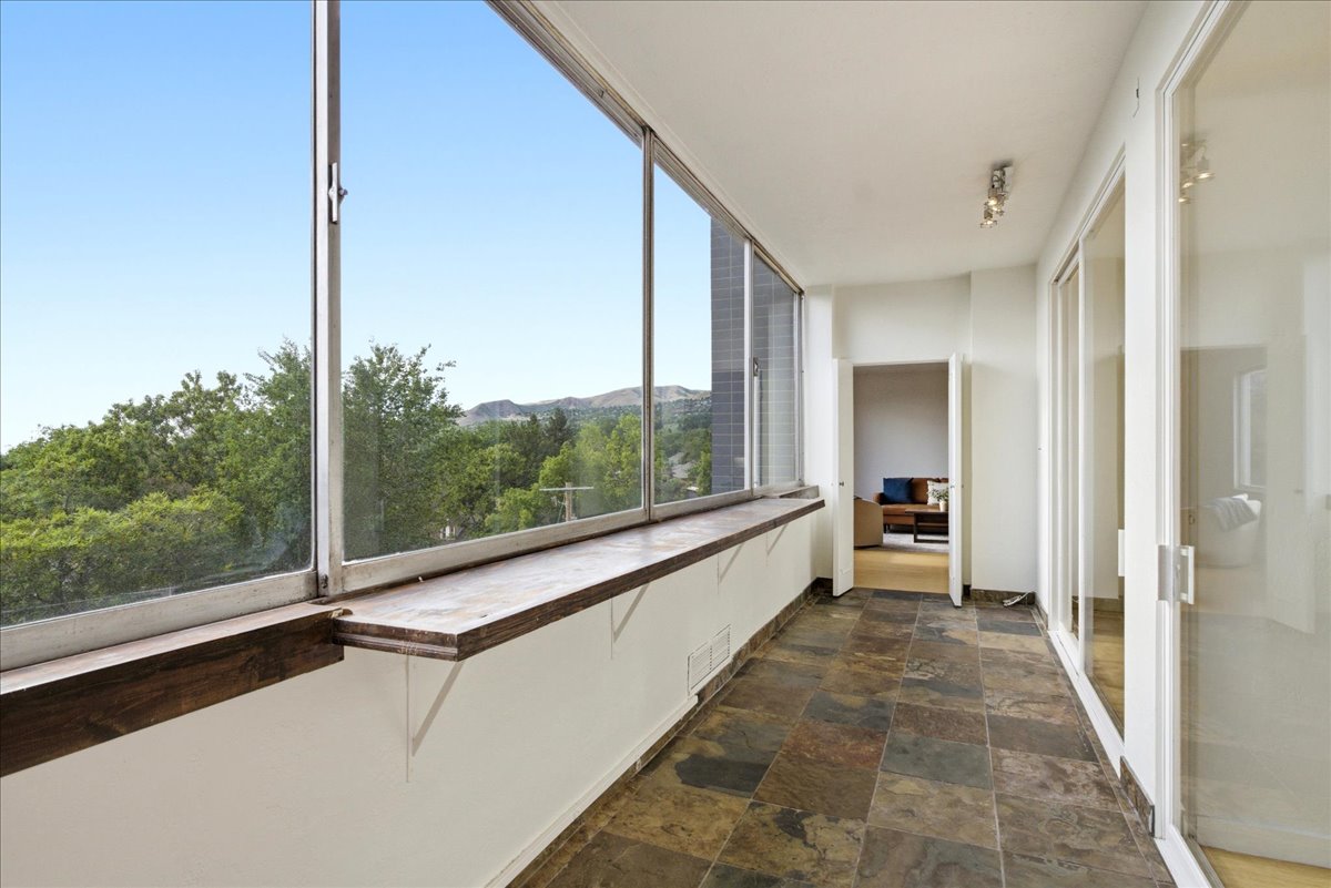 Enclosed sunroom featuring expansive windows, natural stone tile flooring, a built-in wood window shelf, and track lighting