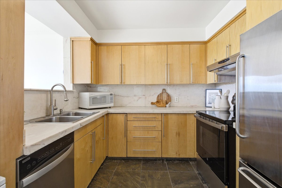 Kitchen featuring natural wood cabinetry, stone countertops, stainless steel appliances, a double basin sink, and dark tile flooring