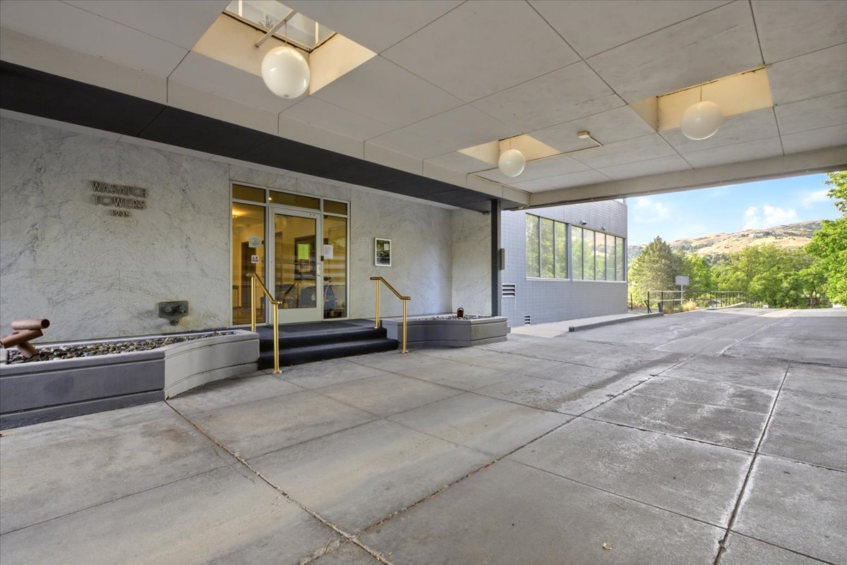 Covered entryway with concrete flooring, accented by a textured facade and gold-toned handrails