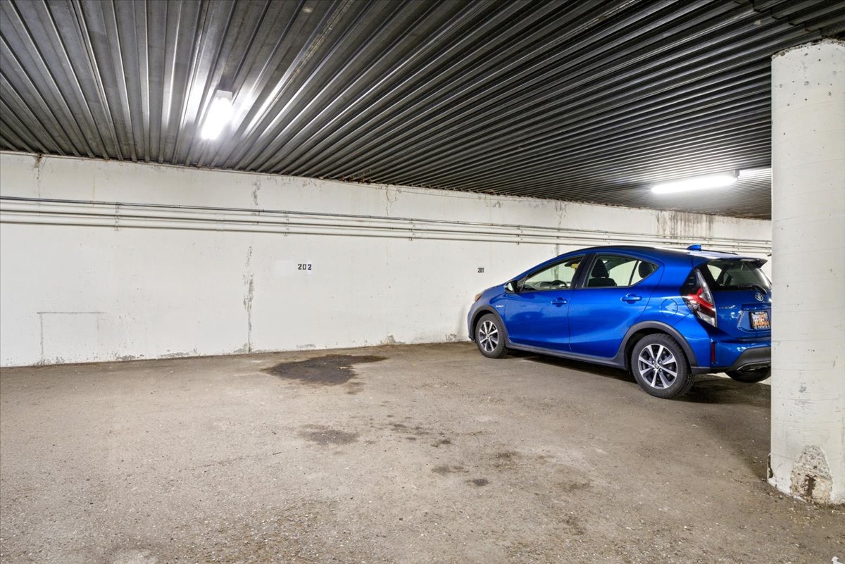 Designated parking space featuring concrete flooring, painted block walls, and a corrugated metal ceiling with fluorescent lighting