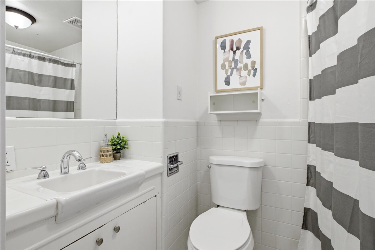 Bathroom featuring white tiled walls, a white vanity with an integrated sink, polished chrome faucet, and a wall-mounted mirror