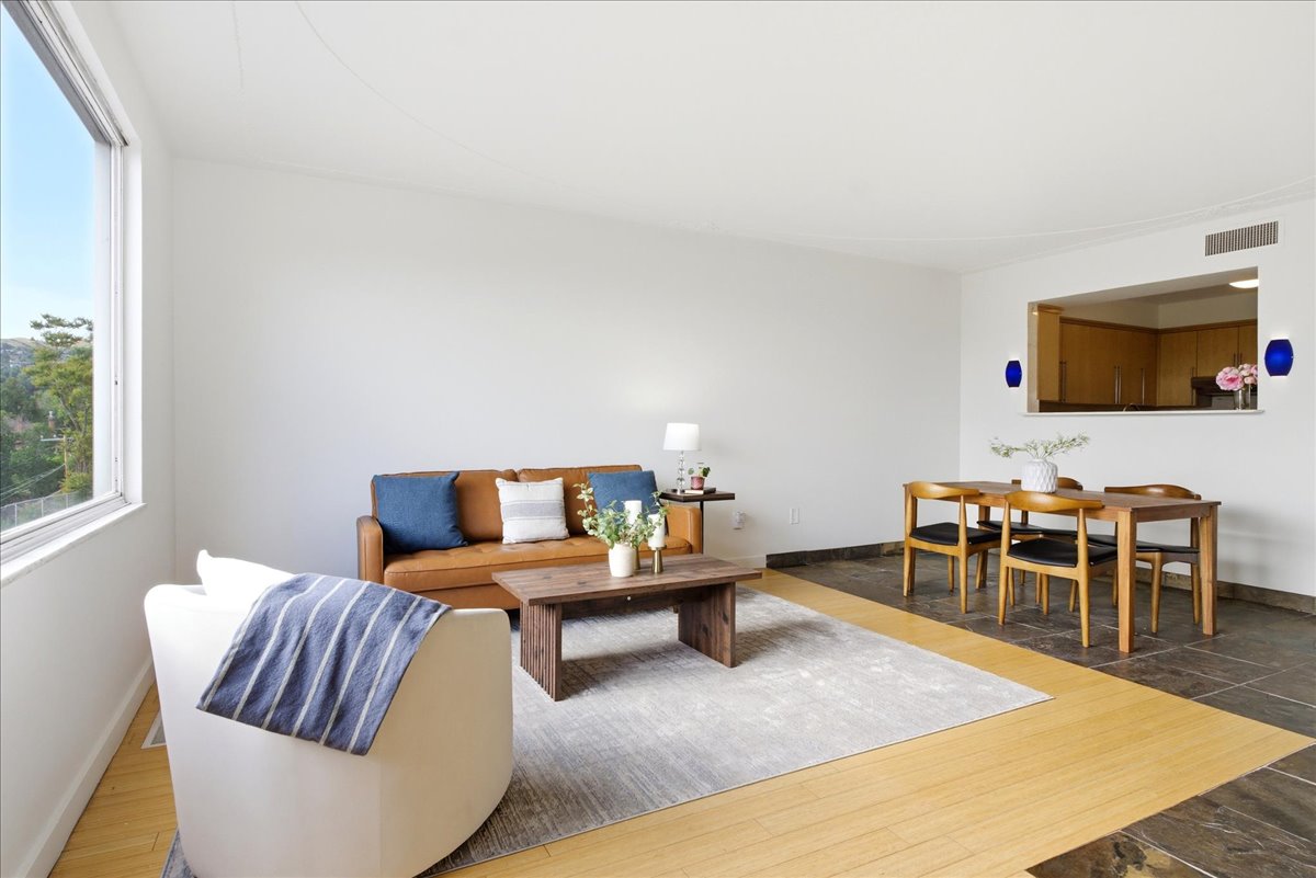Open-concept living area featuring a large window, light wood-finish flooring, and a pass-through opening to the kitchen
