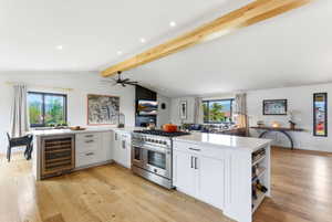 Open-concept kitchen featuring white cabinetry, quartz countertops, a built-in wine refrigerator, stainless steel range with double ovens, and wood-finish flooring