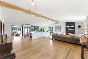 Spacious open-concept living area featuring light wood-finish flooring, vaulted ceilings with exposed wood beams, and recessed lighting