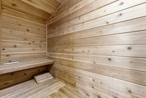 Interior sauna room featuring horizontal wood paneling, built-in benches, and sloped ceiling