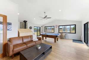 Spacious room featuring vaulted ceilings, light wood-finish flooring, recessed lighting, and a prominent stone-clad fireplace with a black stovepipe