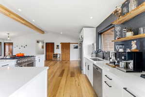 Open-concept kitchen featuring white cabinetry, stainless steel appliances, a large range with multiple burners, wood-finish flooring, and exposed ceiling beams