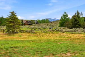 Expansive green space featuring a split-rail fence, mature evergreen trees, and distant mountain scenery