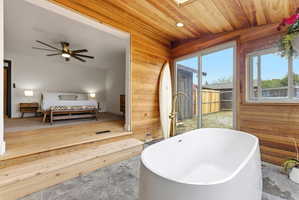 Freestanding soaking tub with a floor-mounted gold-tone faucet, wood-paneled walls and ceiling, skylight, and large sliding glass door