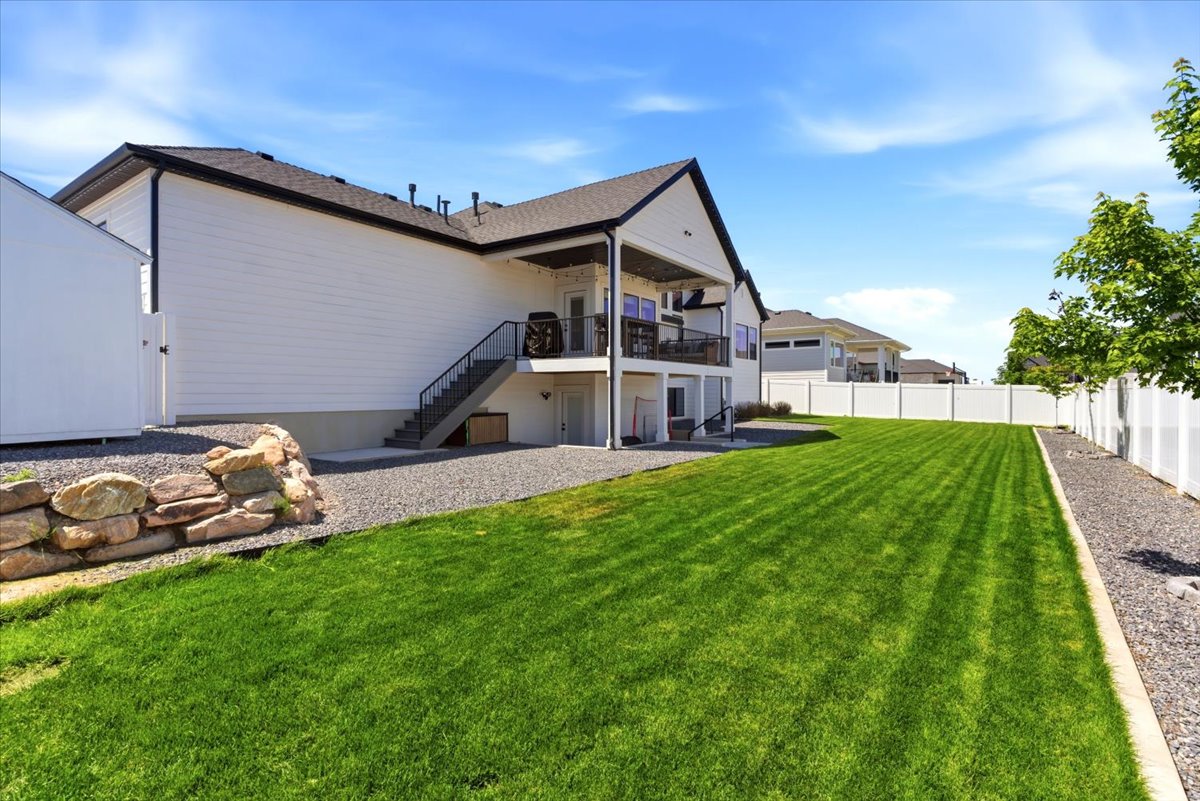Expansive backyard featuring a large green lawn, and white privacy fencing