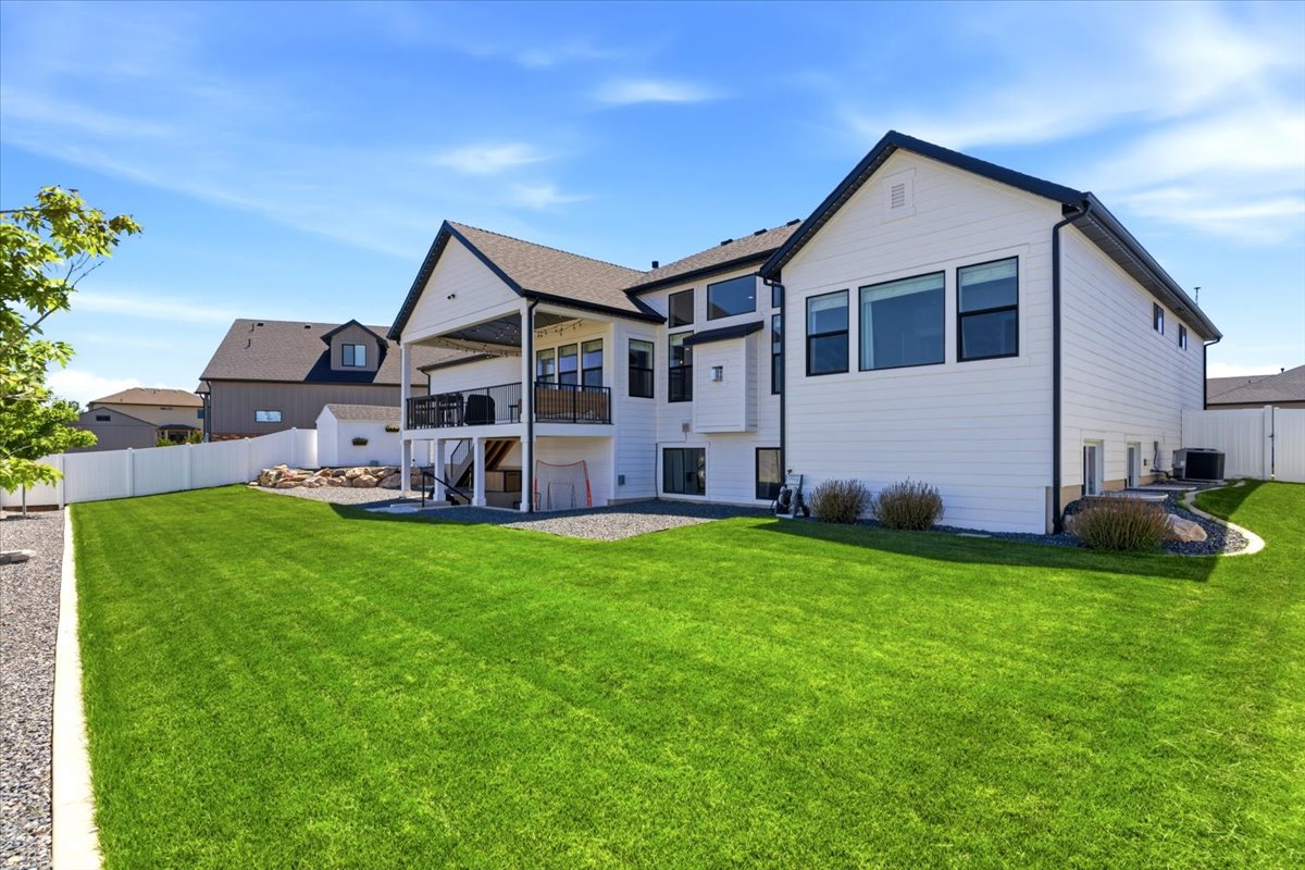 Expansive backyard featuring a lush lawn, white privacy fencing, and a deck with a patio below and black iron railing