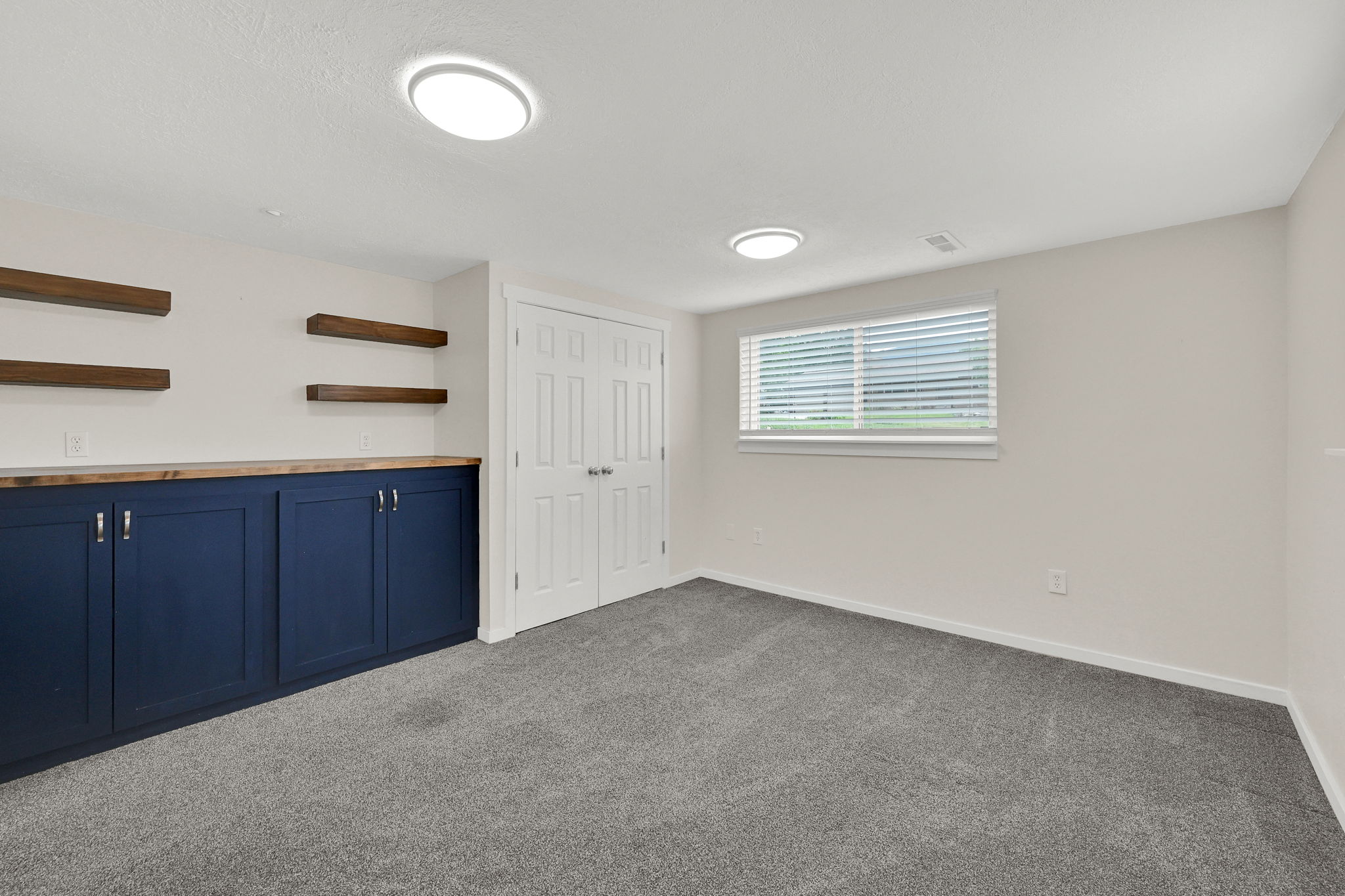 Finished room featuring built-in navy cabinetry with wood-finish countertop, floating wood-finish shelving, and neutral gray carpeting