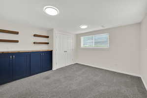 Finished room featuring built-in navy cabinetry with wood-finish countertop, floating wood-finish shelving, and neutral gray carpeting