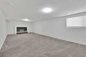 Spacious room with a brick-clad fireplace and hearth, neutral carpet, white walls, and a window with blinds