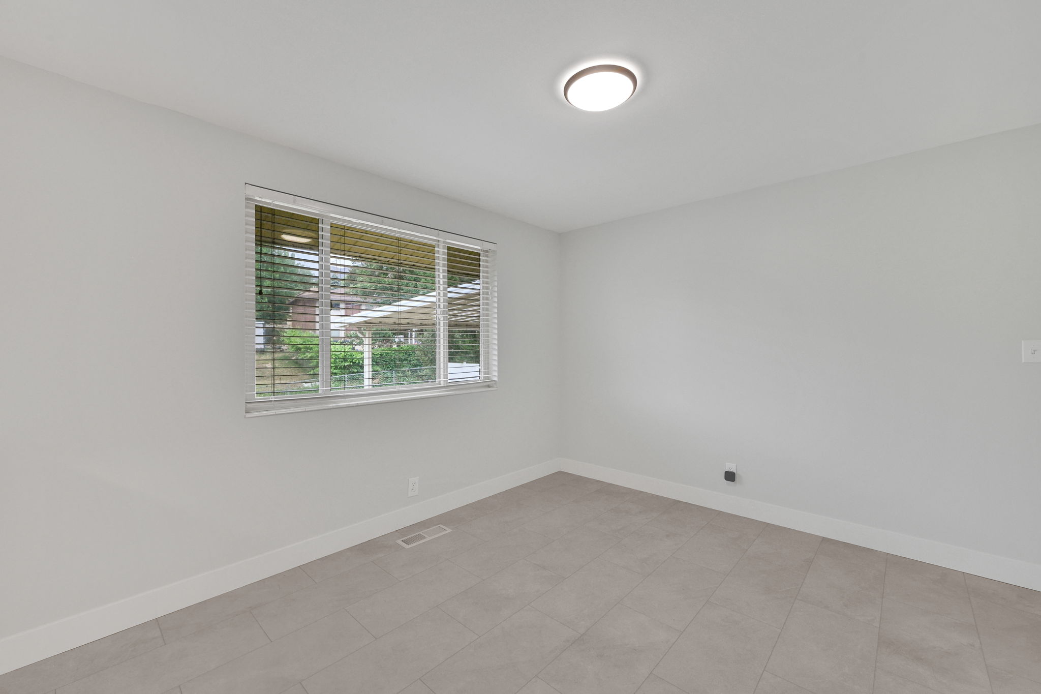 Neutral tone wall paint, contemporary flush-mount ceiling light, white baseboards, and window with horizontal blinds