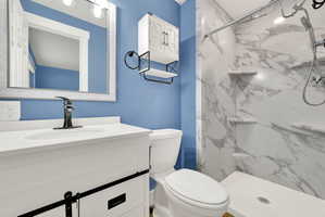 Bathroom featuring a walk-in shower with marble-look wall panels and built-in shelving, a white vanity with a single basin sink and black faucet, a framed mirror, and a wall-mounted storage cabinet