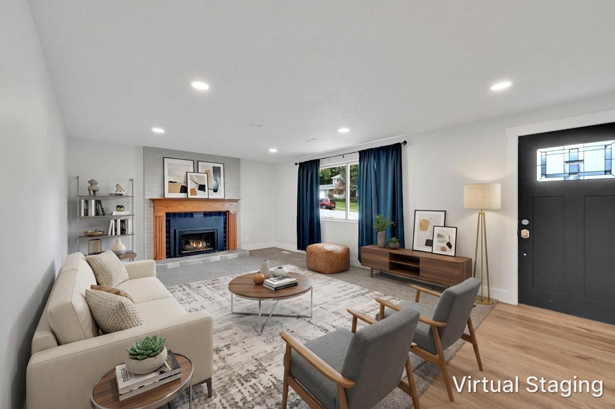 Living area featuring a fireplace with a wood mantle and tile surround, recessed lighting, wood-finish flooring, a contemporary dark entry door with a transom window, and windows with dark-colored curtains. Room was virtually staged.