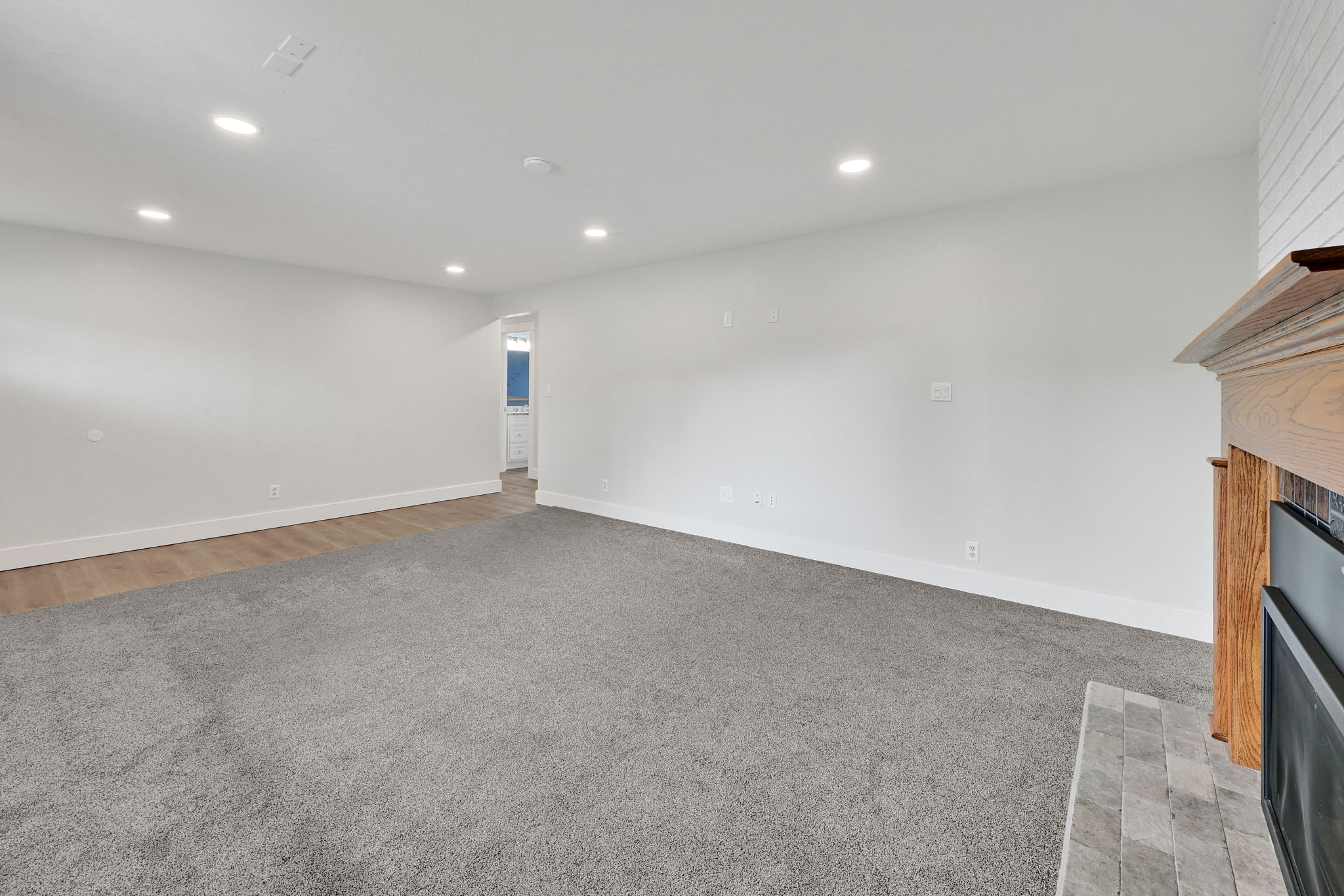 Spacious living area featuring neutral carpeting, recessed lighting, wood-finish flooring, a fireplace with a wood mantle, and a tile hearth