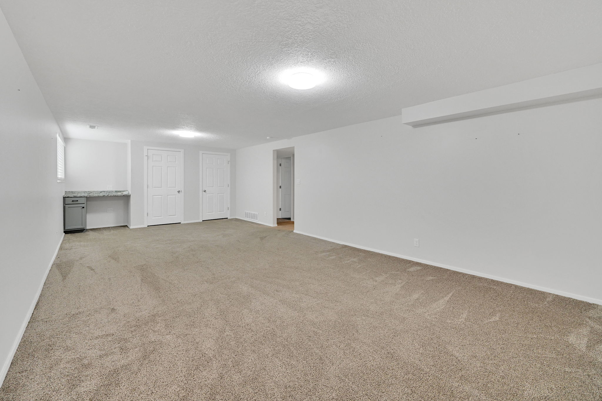 Spacious carpeted room featuring a built-in desk with a light-colored countertop, two panel doors, and recessed lighting