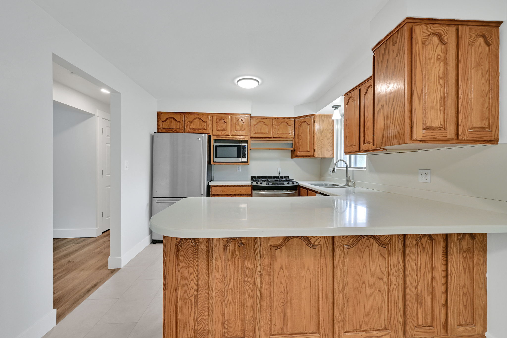 Kitchen featuring wood cabinetry, light-toned countertops, stainless steel appliances, and tile flooring