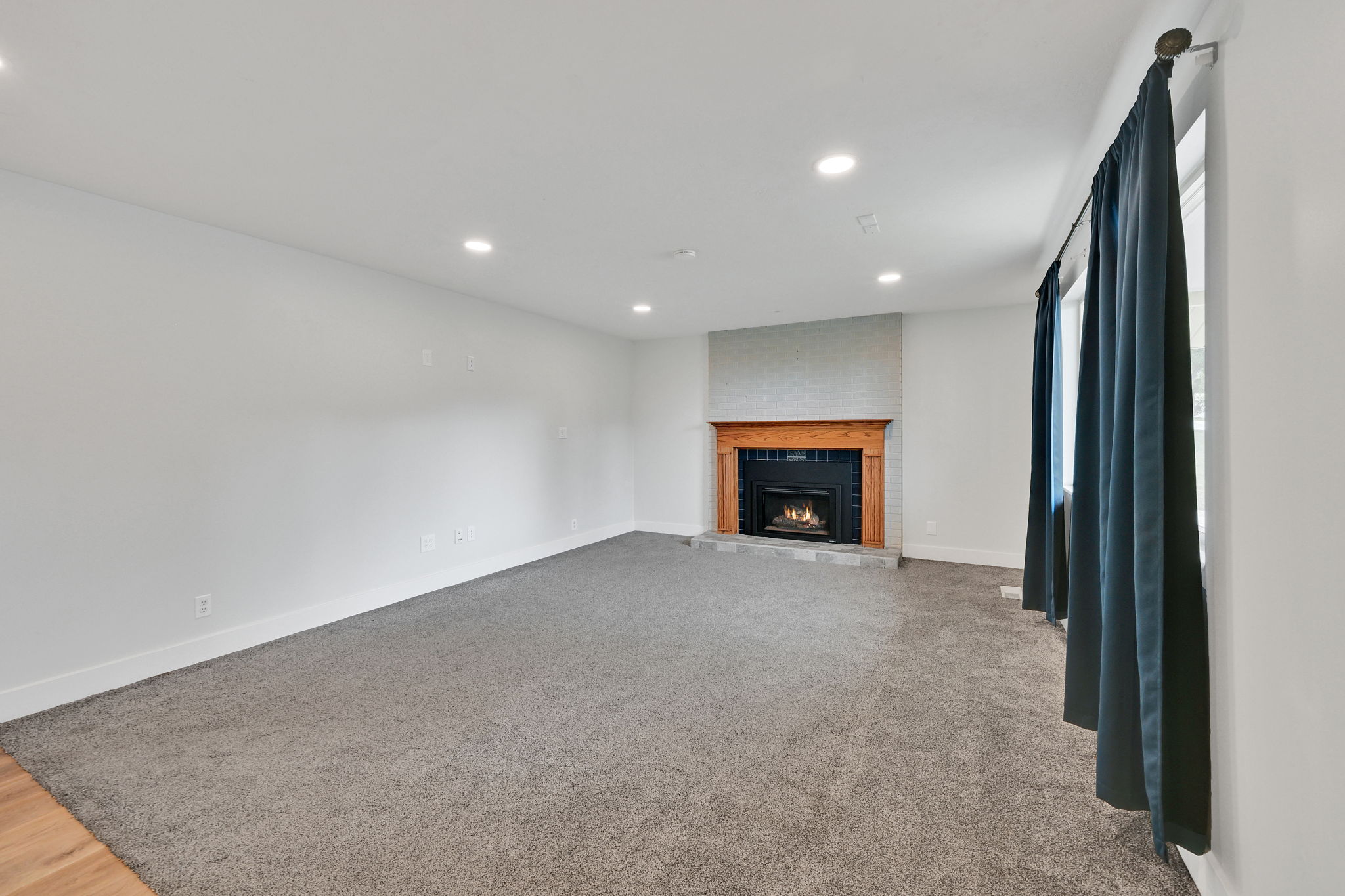 Living space featuring a fireplace with a wood mantle and stone surround, recessed lighting, gray carpeting, and white baseboards