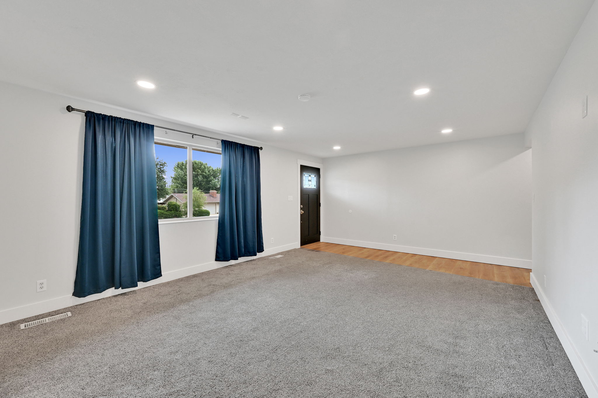 Spacious room featuring gray carpet, white walls, recessed lighting, and a window with white trim
