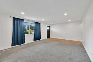 Spacious room featuring gray carpet, white walls, recessed lighting, and a window with white trim